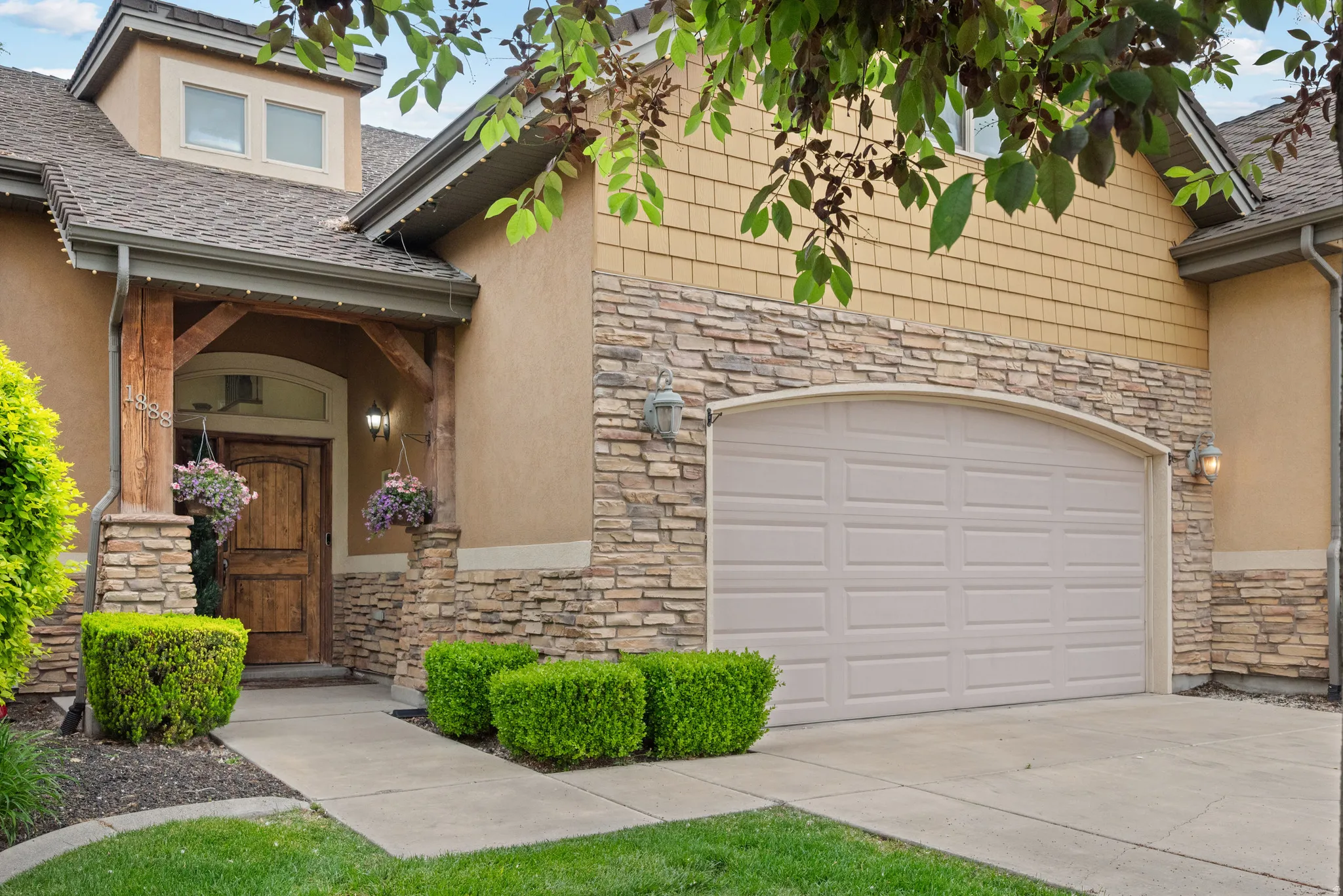 Exterior facade featuring a stone veneer and stucco finish, a wood-finish entry door, an arched garage door, and a dormer window