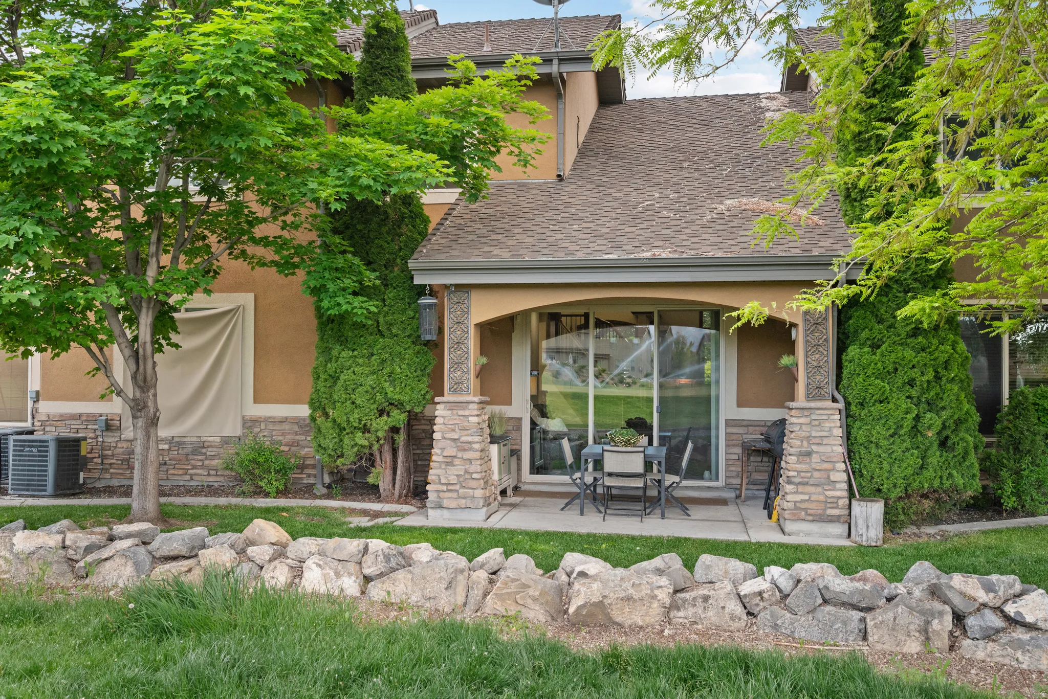 Rear patio featuring a covered area with stone-clad columns, sliding glass doors, and a concrete surface
