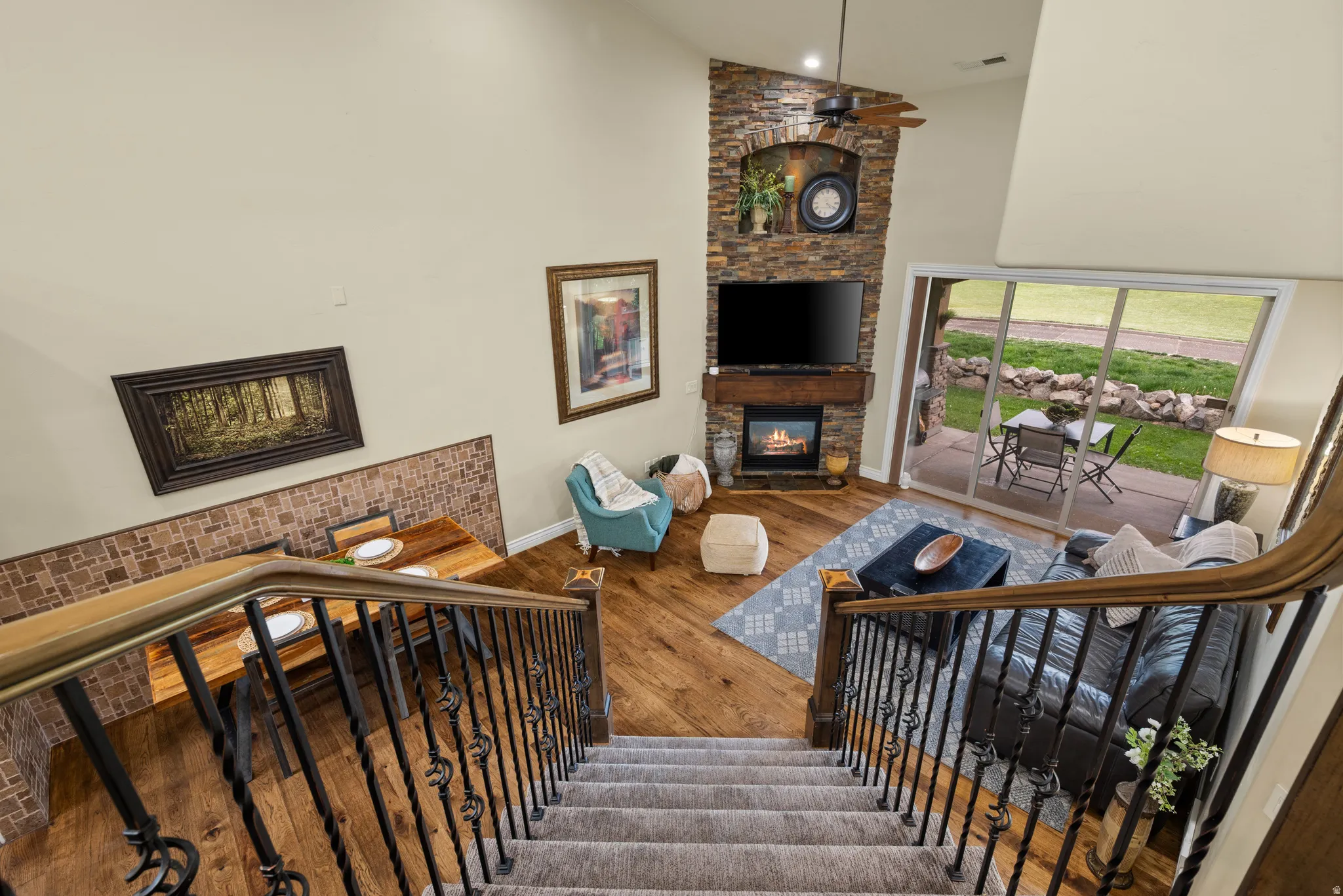 Open-concept living space featuring wood-finish flooring, a stone-clad fireplace with a wood mantle, and sliding glass doors to the patio