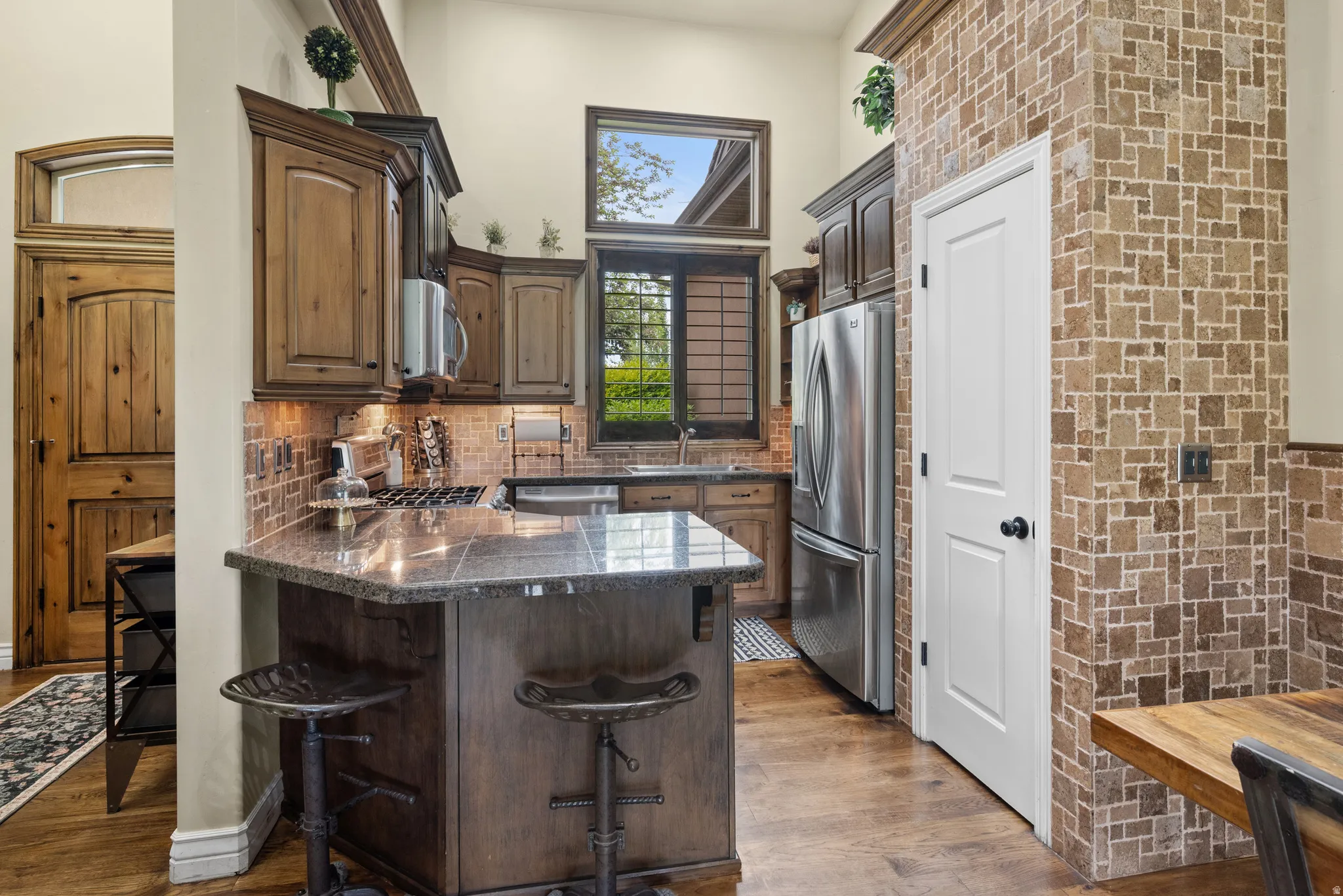 Gourmet kitchen featuring wood-finish cabinetry, stainless steel appliances, a stone countertop island, mosaic tile backsplash, and wood-finish flooring