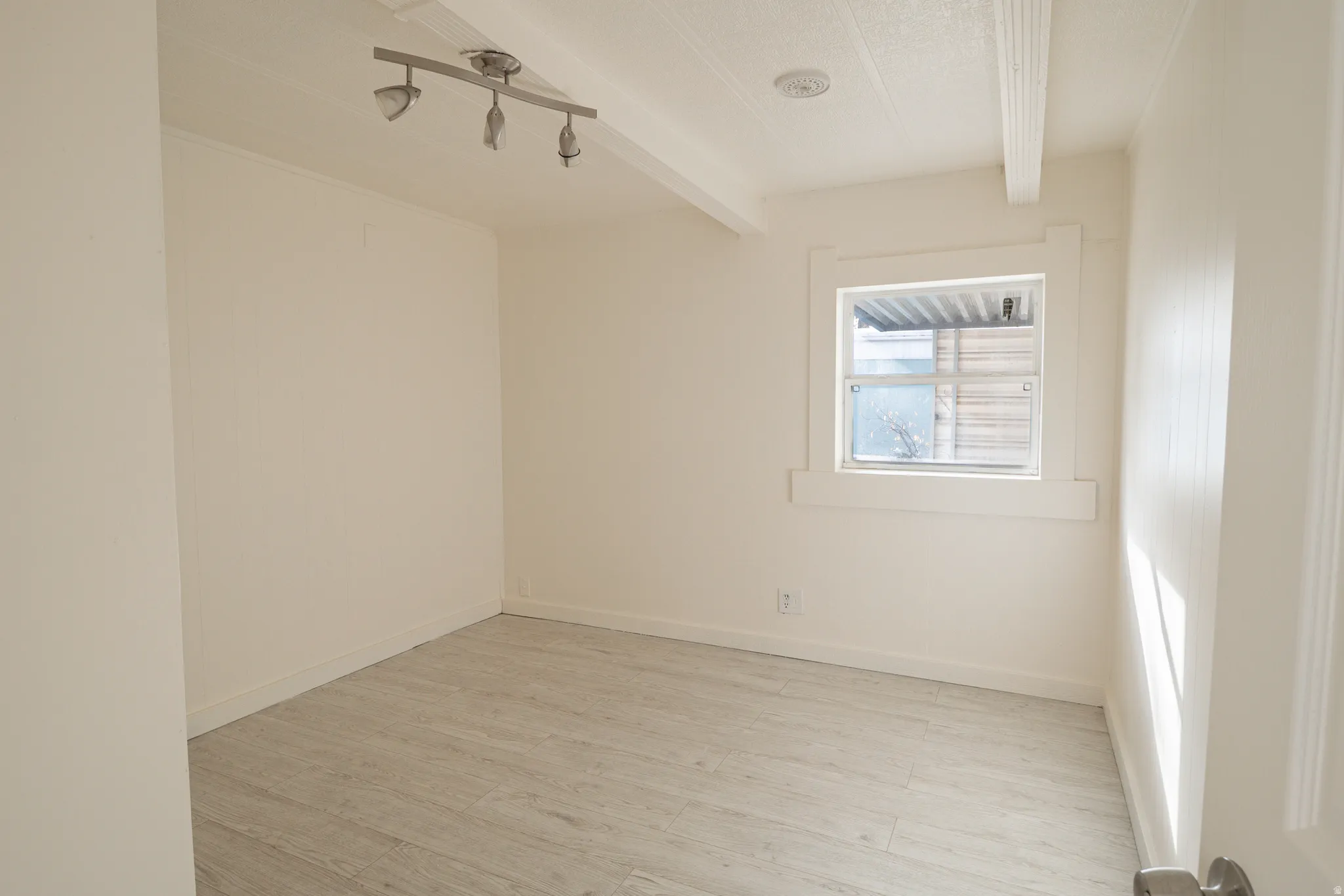 Room featuring wood-finish flooring, a window with white trim, and a ceiling-mounted track light fixture