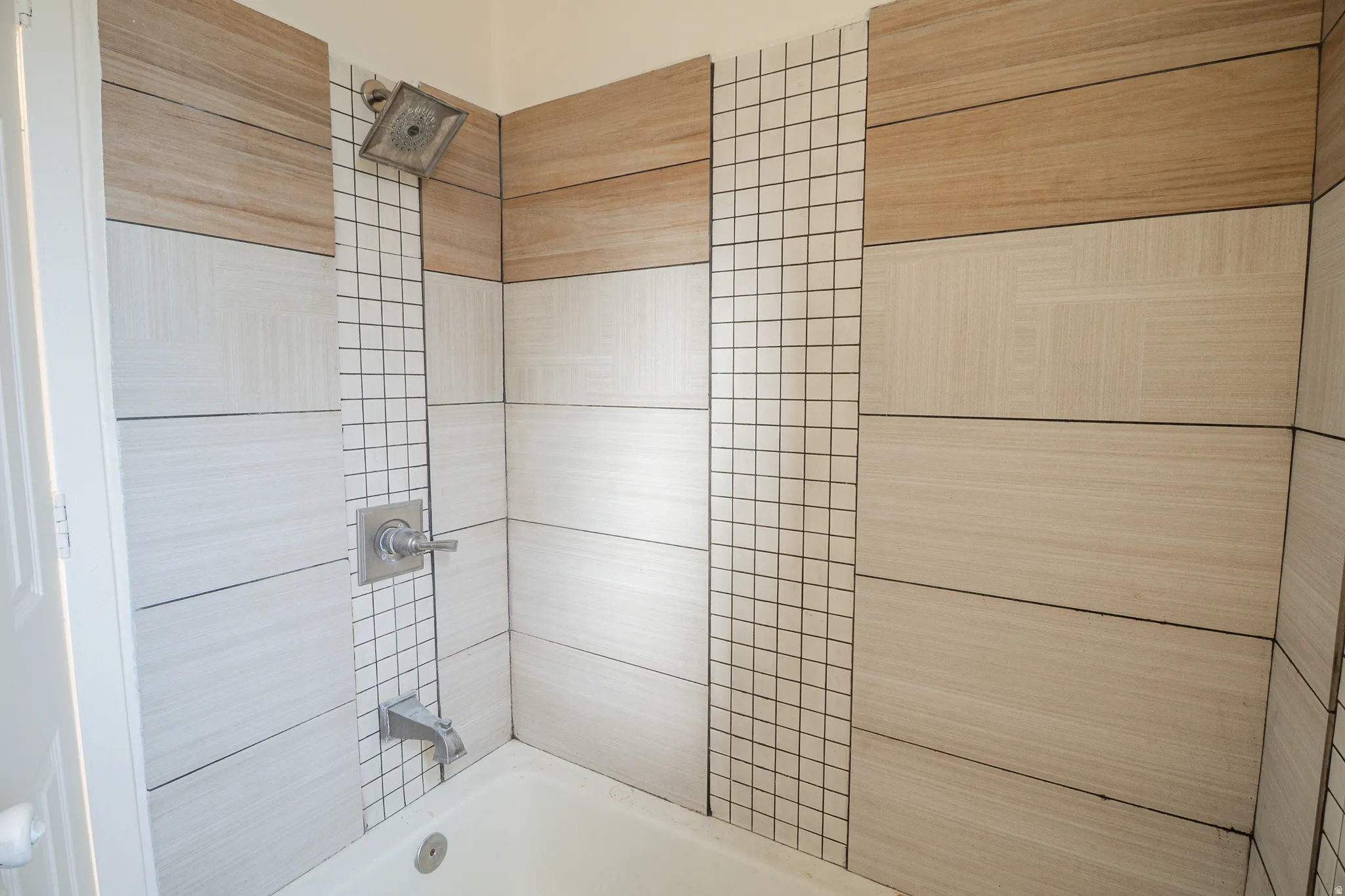 Bathtub and shower combination featuring a rain showerhead, brushed nickel fixtures, wood-finish tile accents, and a vertical mosaic tile stripe