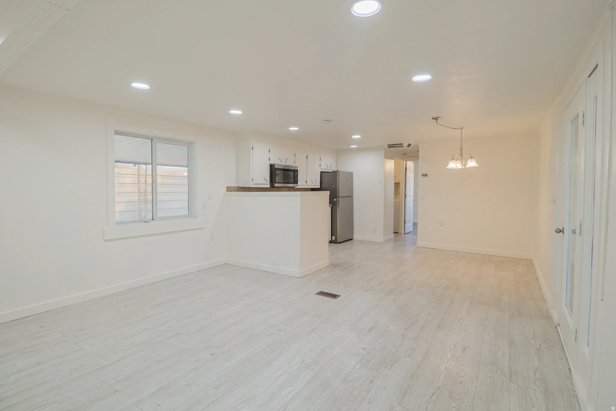 Open-concept living area featuring light wood-finish flooring, recessed lighting, and a kitchen pass-through with wood countertop