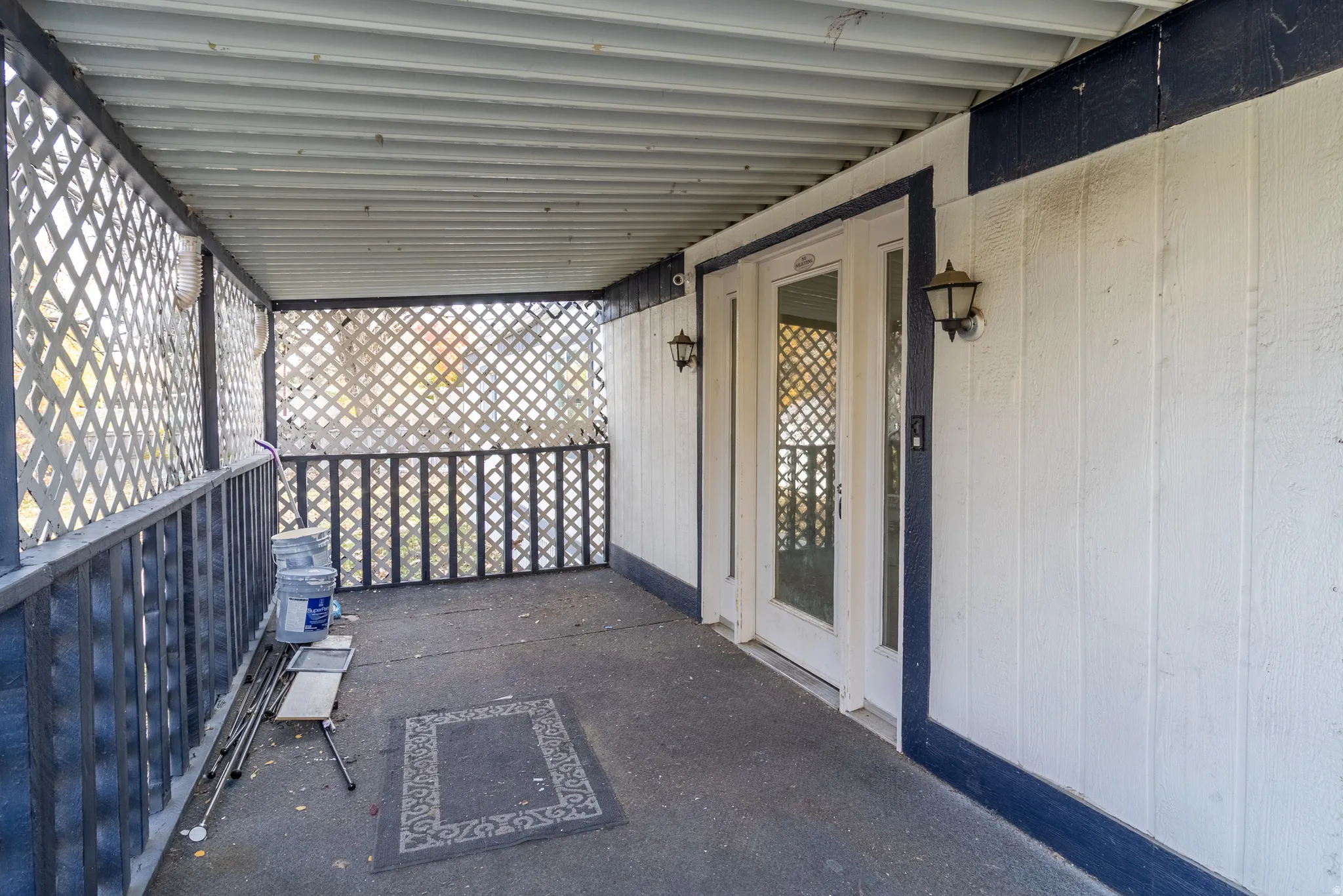 Covered porch with lattice railing, twin glass-paned doors, and exterior wall sconces