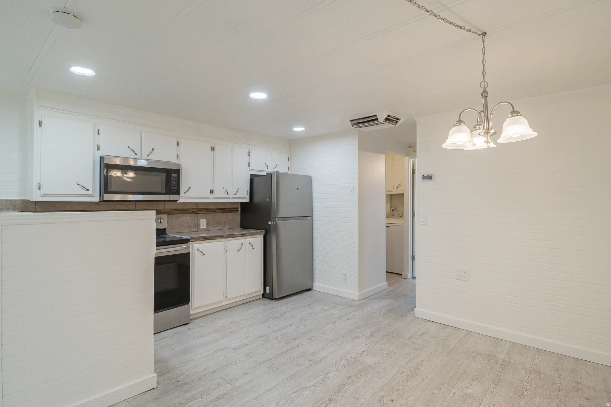 Kitchen and dining area featuring stainless steel appliances, white cabinetry, light wood-finish flooring, a chandelier, and recessed lighting