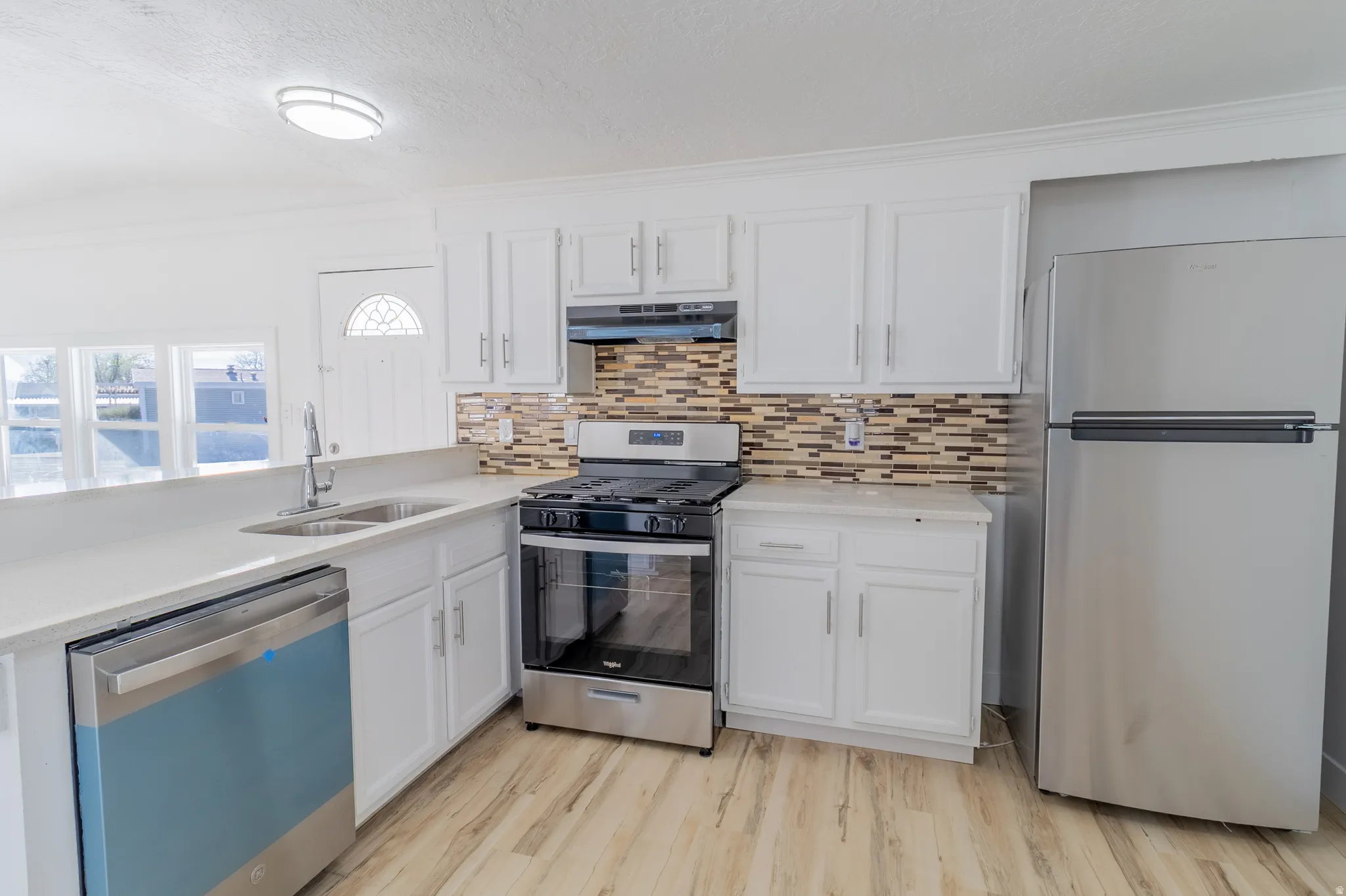 Kitchen featuring white cabinetry, stainless steel appliances, a mosaic tile backsplash, light-toned countertops, and wood-finish flooring