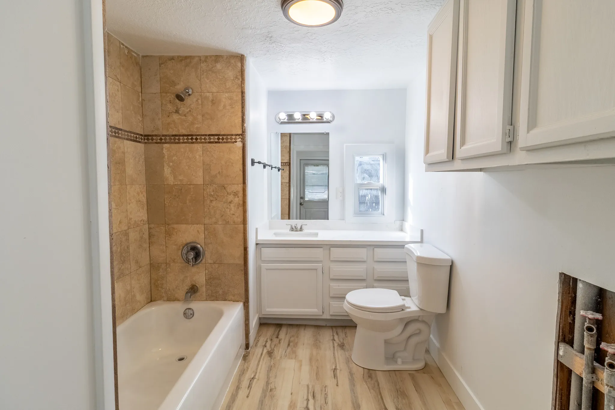 Bathroom featuring a tiled shower/tub combination, a vanity with a white countertop and base cabinetry, wood-finish flooring, and a window