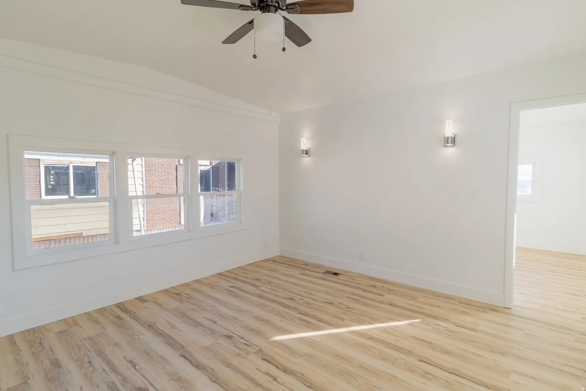 Bright interior space featuring light wood-finish flooring, white walls, and a ceiling fan with integrated lighting