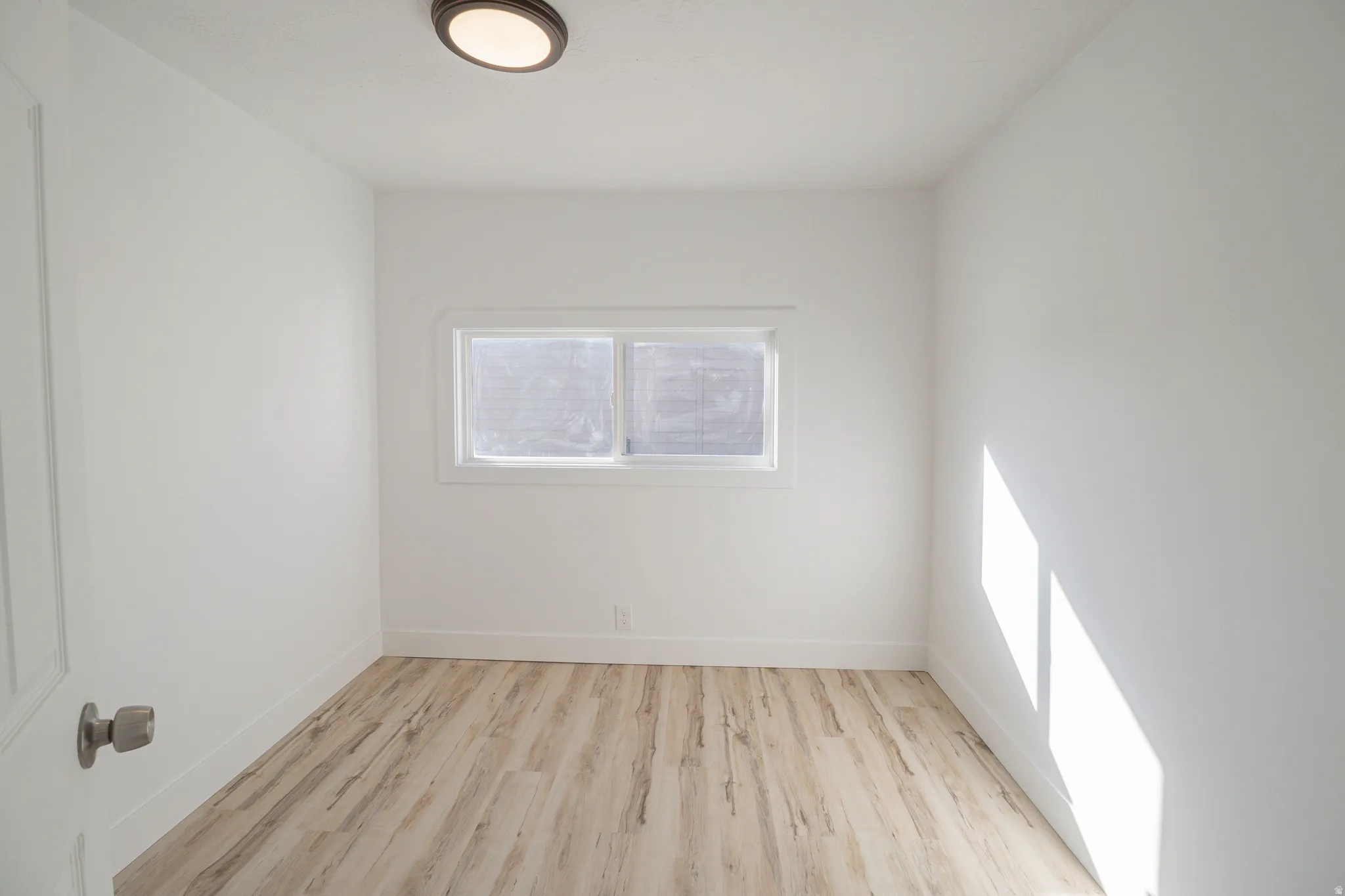 Room featuring light wood-finish flooring, white walls, and a window with white trim