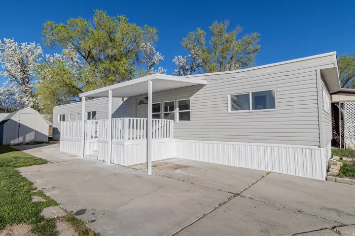 Exterior featuring light gray siding, white skirting, and a covered porch with white railing