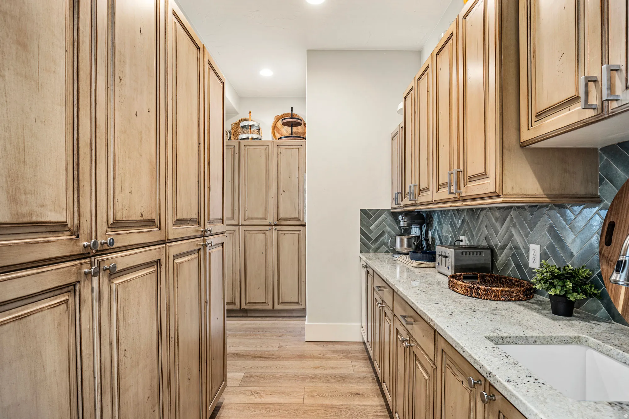 Galley kitchen featuring extensive natural wood cabinetry, light-toned countertops, a light blue herringbone tile backsplash, and recessed lighting