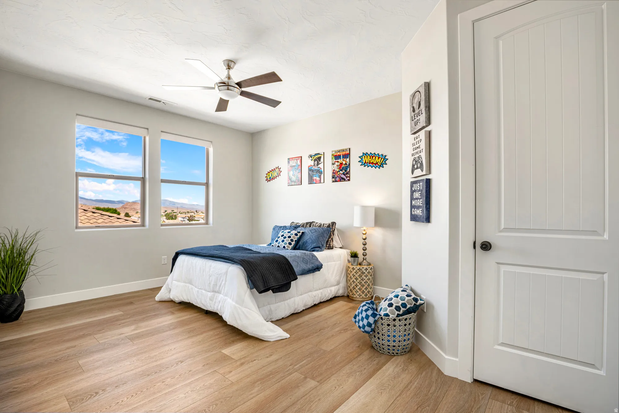 Bright room featuring two large windows, wood-finish flooring, a ceiling fan with integrated lighting, and a white paneled door