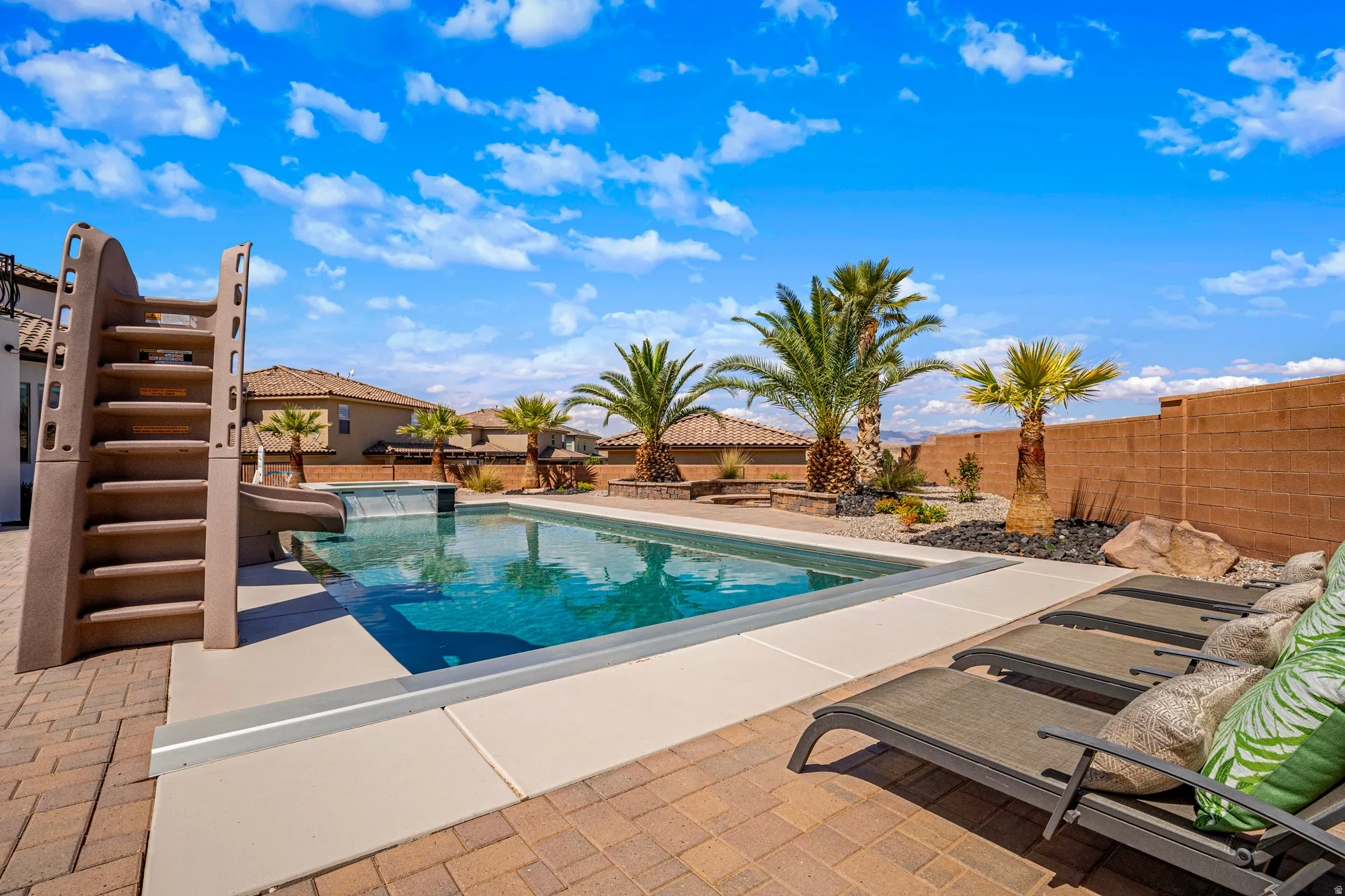 Private backyard featuring a rectangular swimming pool with a waterfall feature, an attached pool slide, paver patio, and mature palm trees