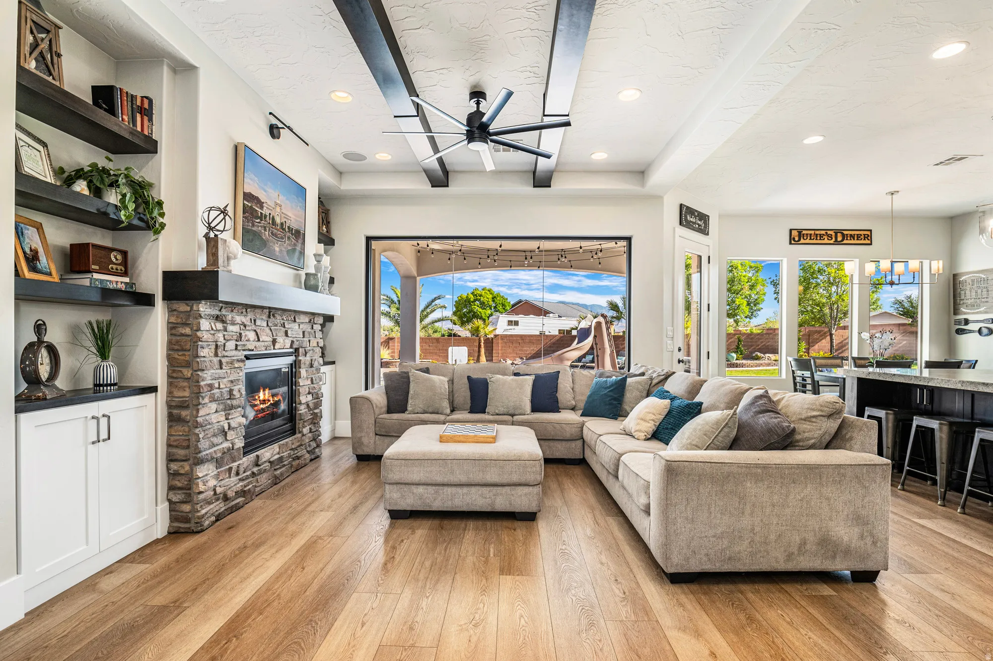 Spacious living area featuring exposed ceiling beams, a stone-clad fireplace with mantel, and wood-finish flooring