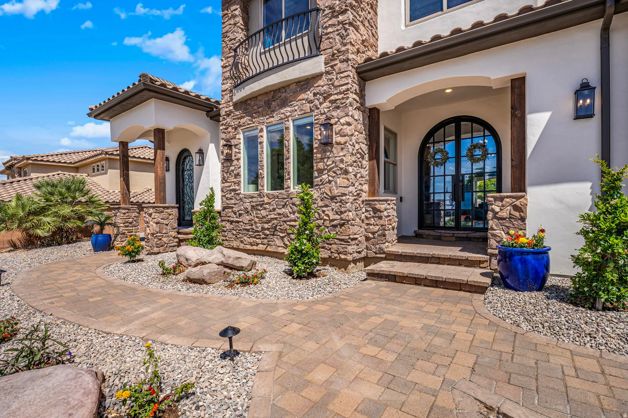 Stone and stucco exterior featuring a grand arched double-door entry with dark framing, a paver walkway, and a stone-clad tower element
