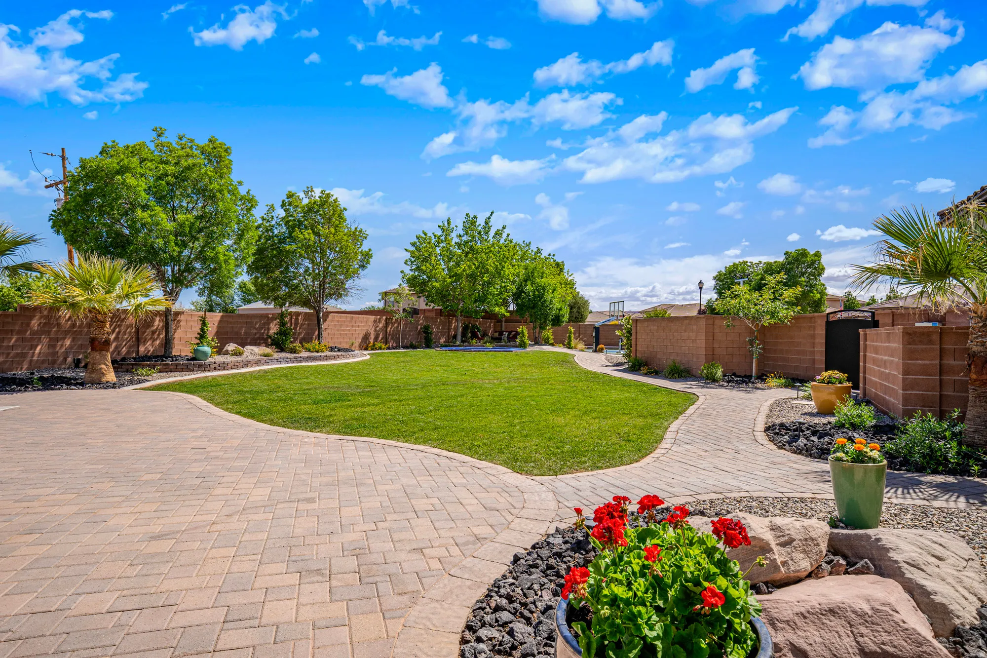 Expansive backyard featuring a large green lawn, paver patio, paver pathways, mature trees, and landscaping with decorative rock