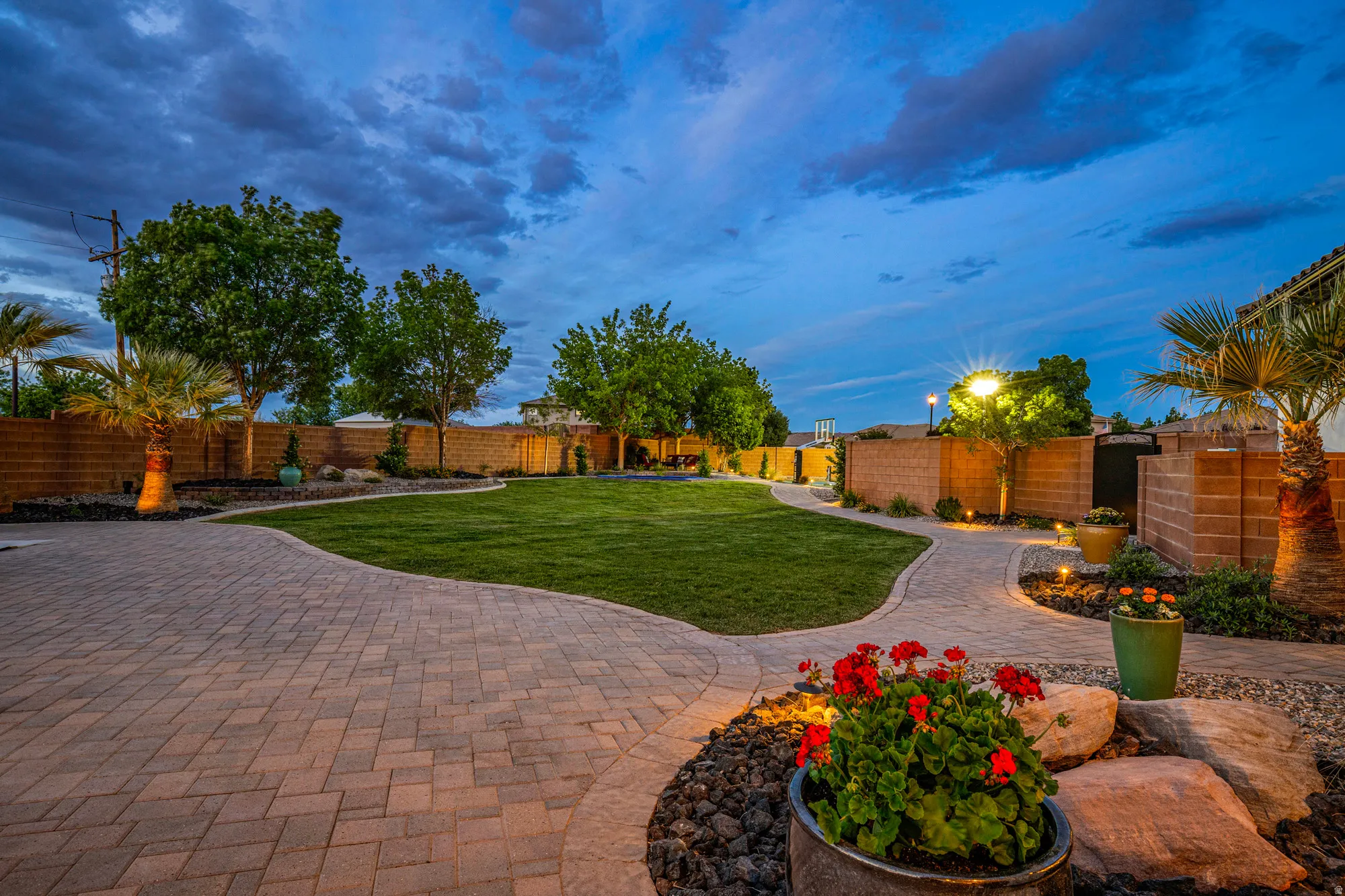 Expansive backyard featuring a large green lawn, paver patio, paver pathways, mature trees, and landscape lighting