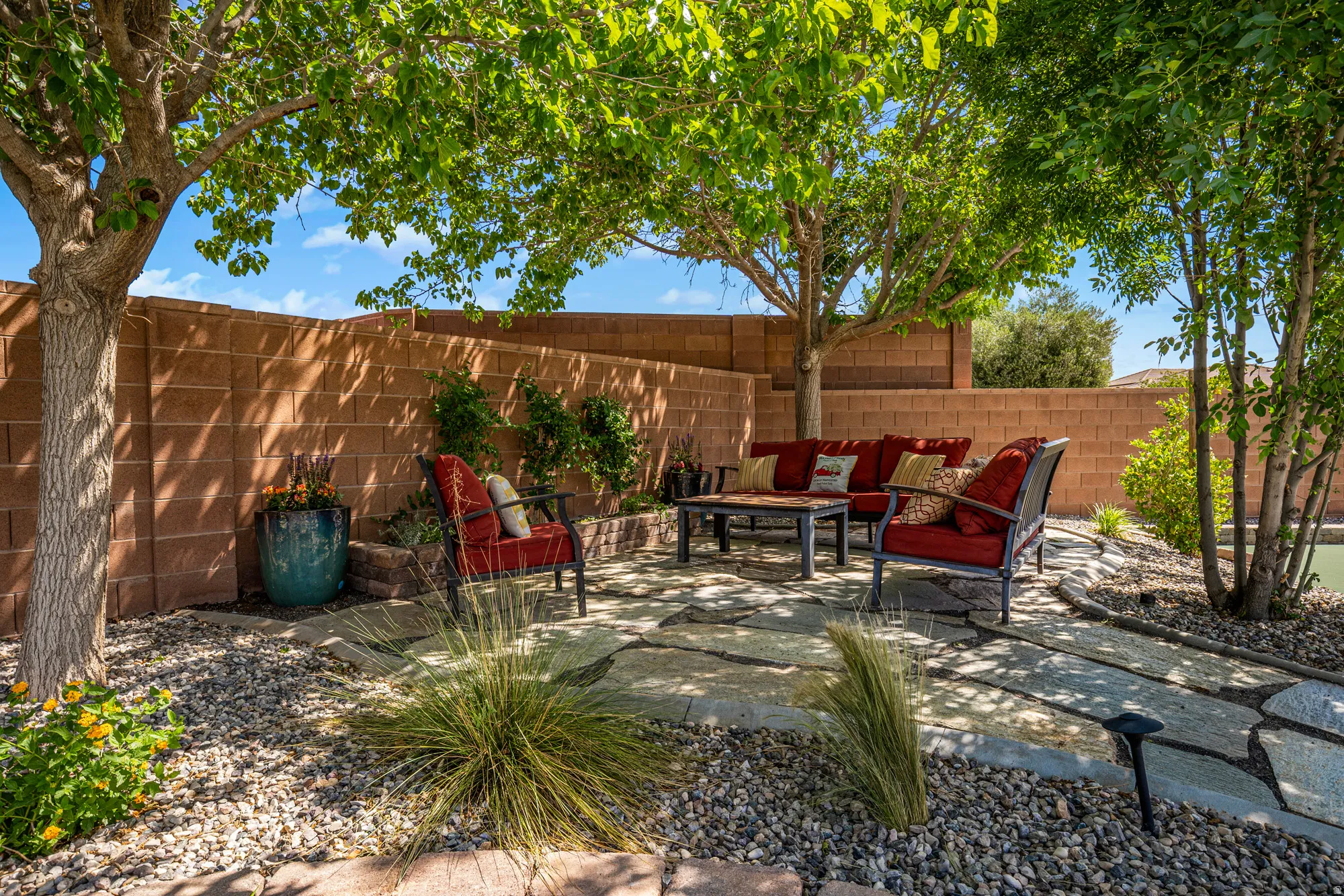 Expansive outdoor patio featuring flagstone paving, surrounding gravel landscaping, mature trees, and a block privacy wall