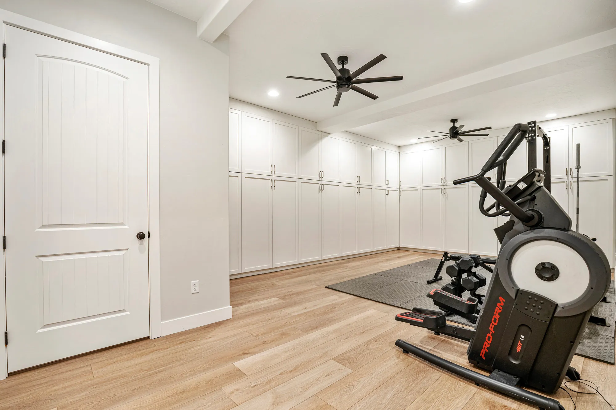 Spacious interior room featuring extensive white built-in cabinetry, light wood-finish flooring, and recessed lighting