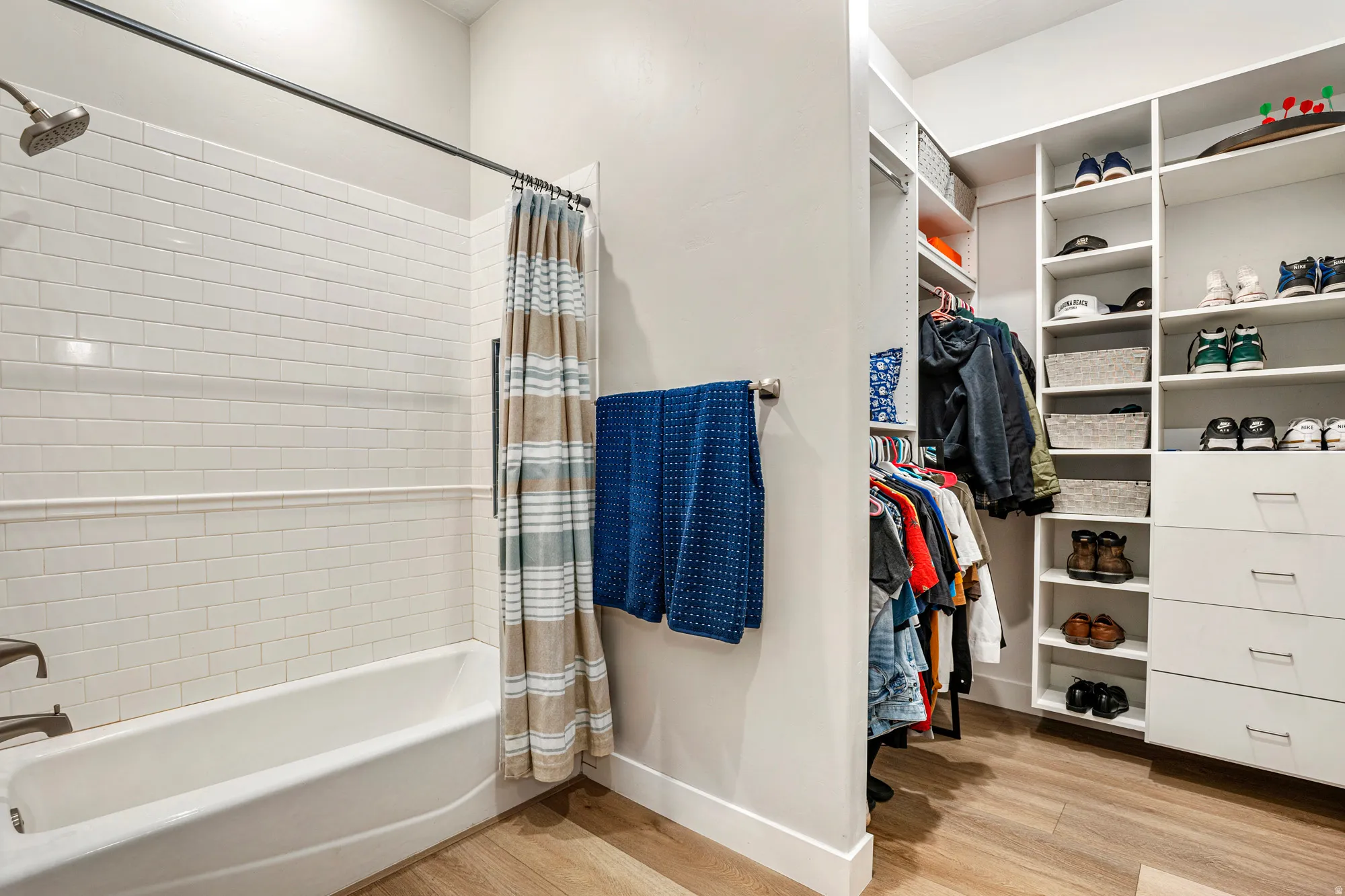 Bathroom featuring a white subway tile shower surround with a built-in tub, a brushed nickel shower head, and a wood-finish floor