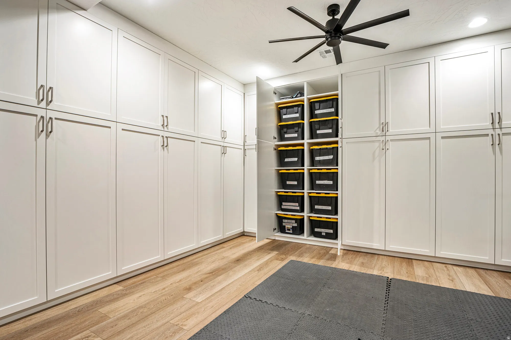 Extensive white built-in cabinetry with brushed nickel hardware, wood-finish flooring, recessed lighting, and a black ceiling fan