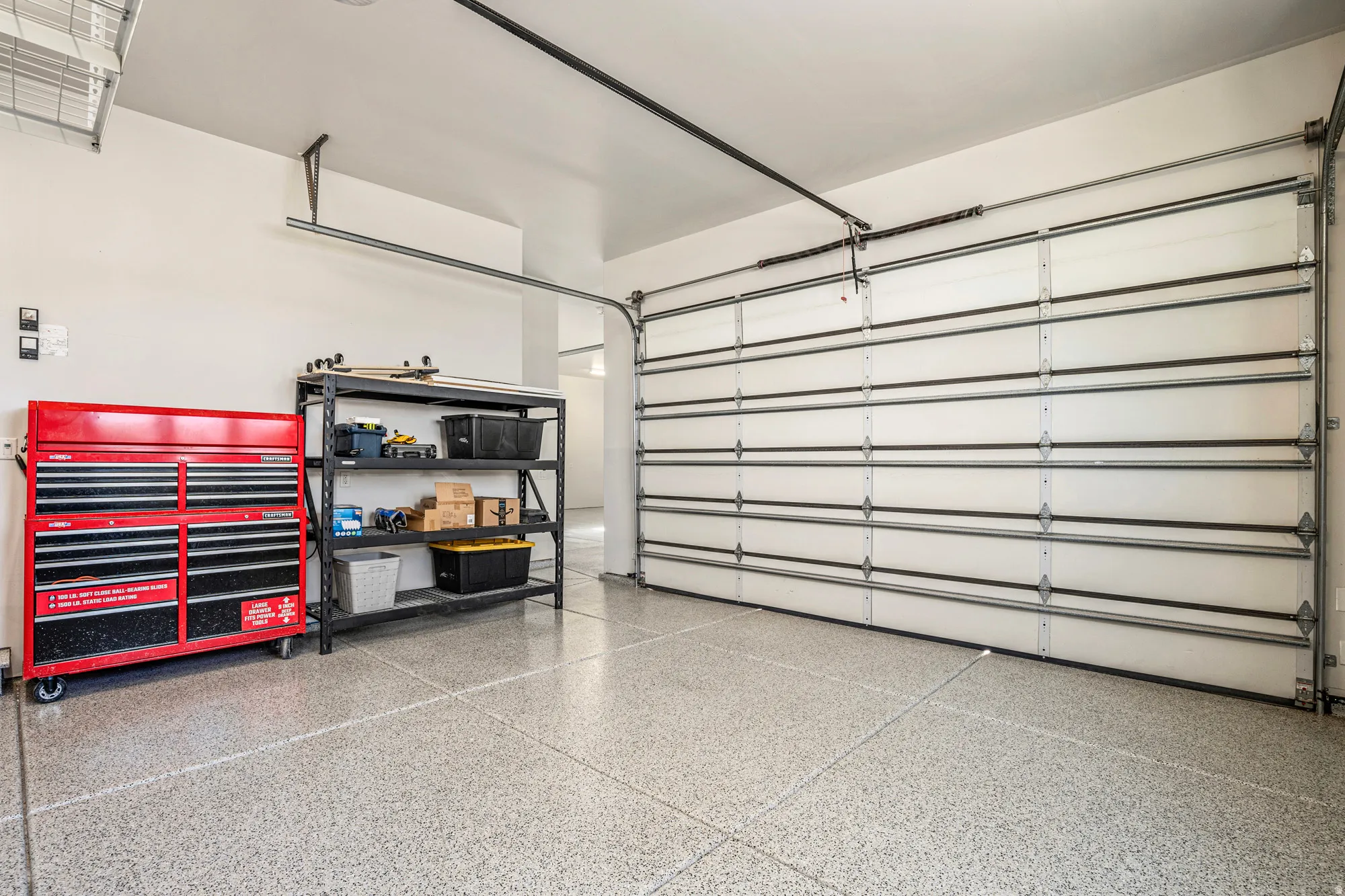 Spacious garage featuring a durable epoxy-coated floor, automatic overhead door, and contemporary white walls