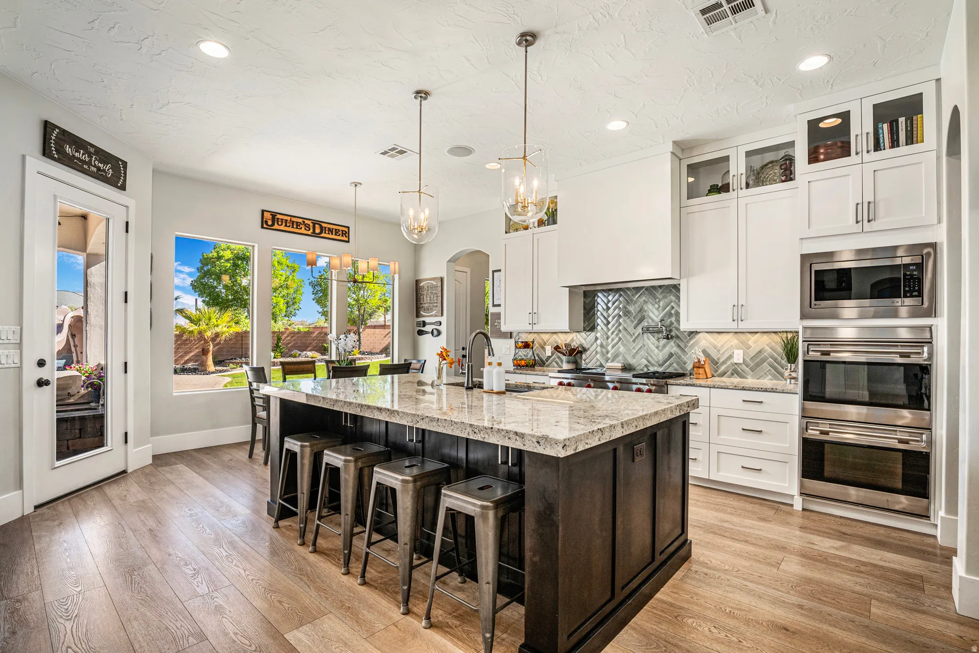 Kitchen featuring a large central island with seating, pendant lighting, stainless steel double ovens, and a herringbone tile backsplash