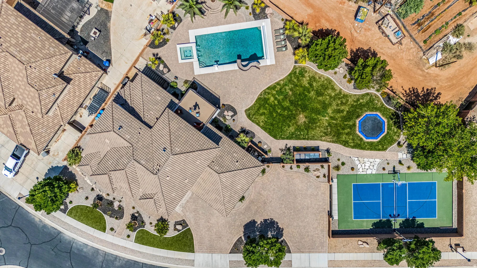 Expansive property featuring a tiled-roof residence, a dedicated tennis court, a large swimming pool with an integrated spa, a manicured lawn area, and mature landscaping