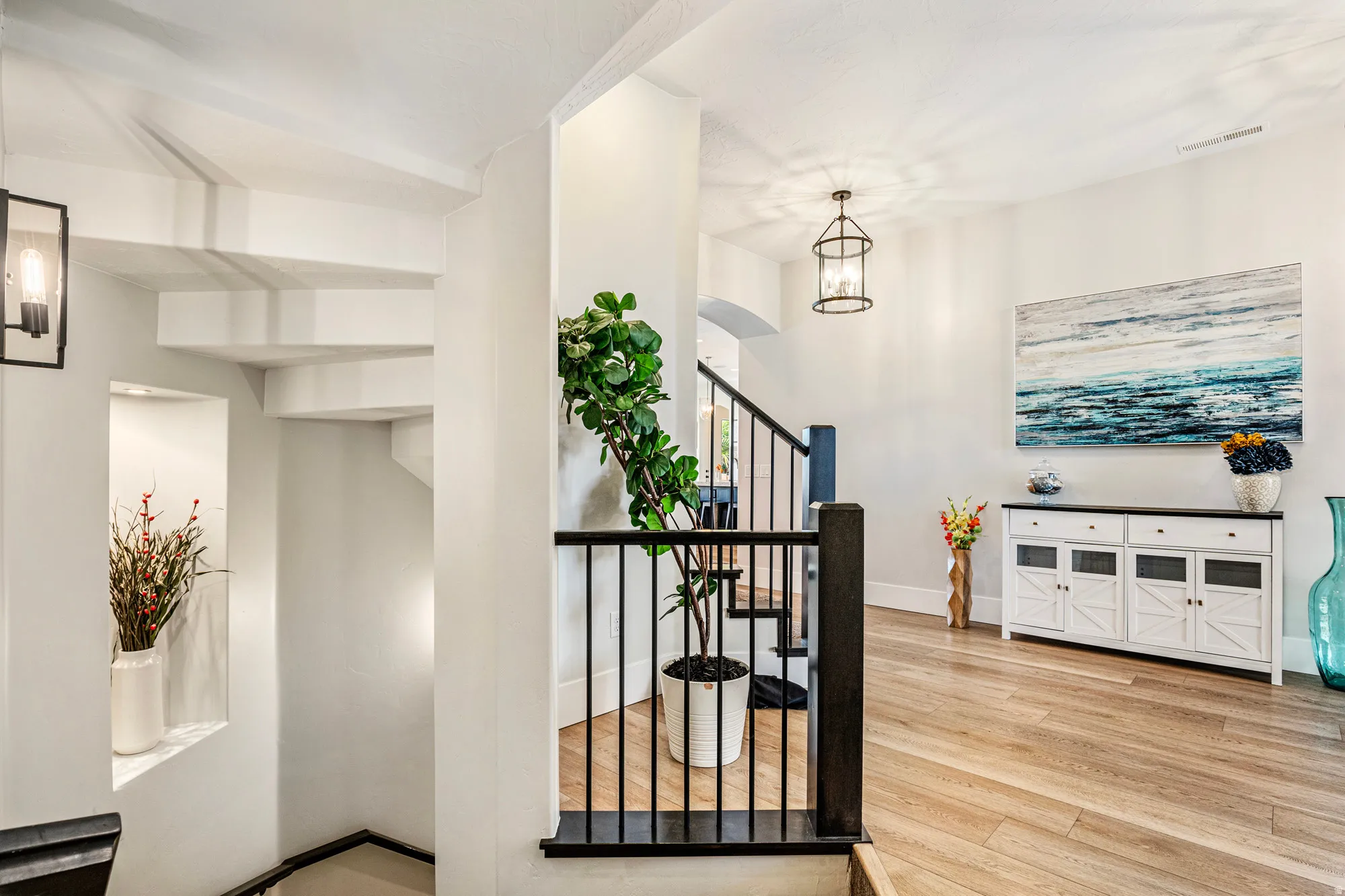 Open-concept entryway featuring wood-finish flooring, a contemporary staircase with black metal balusters and dark wood banister, and a recessed wall niche