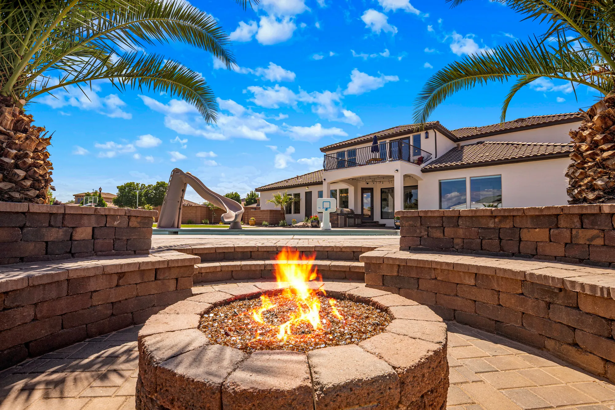 Outdoor hardscape featuring a built-in fire pit with gas logs and surrounding tiered seating walls