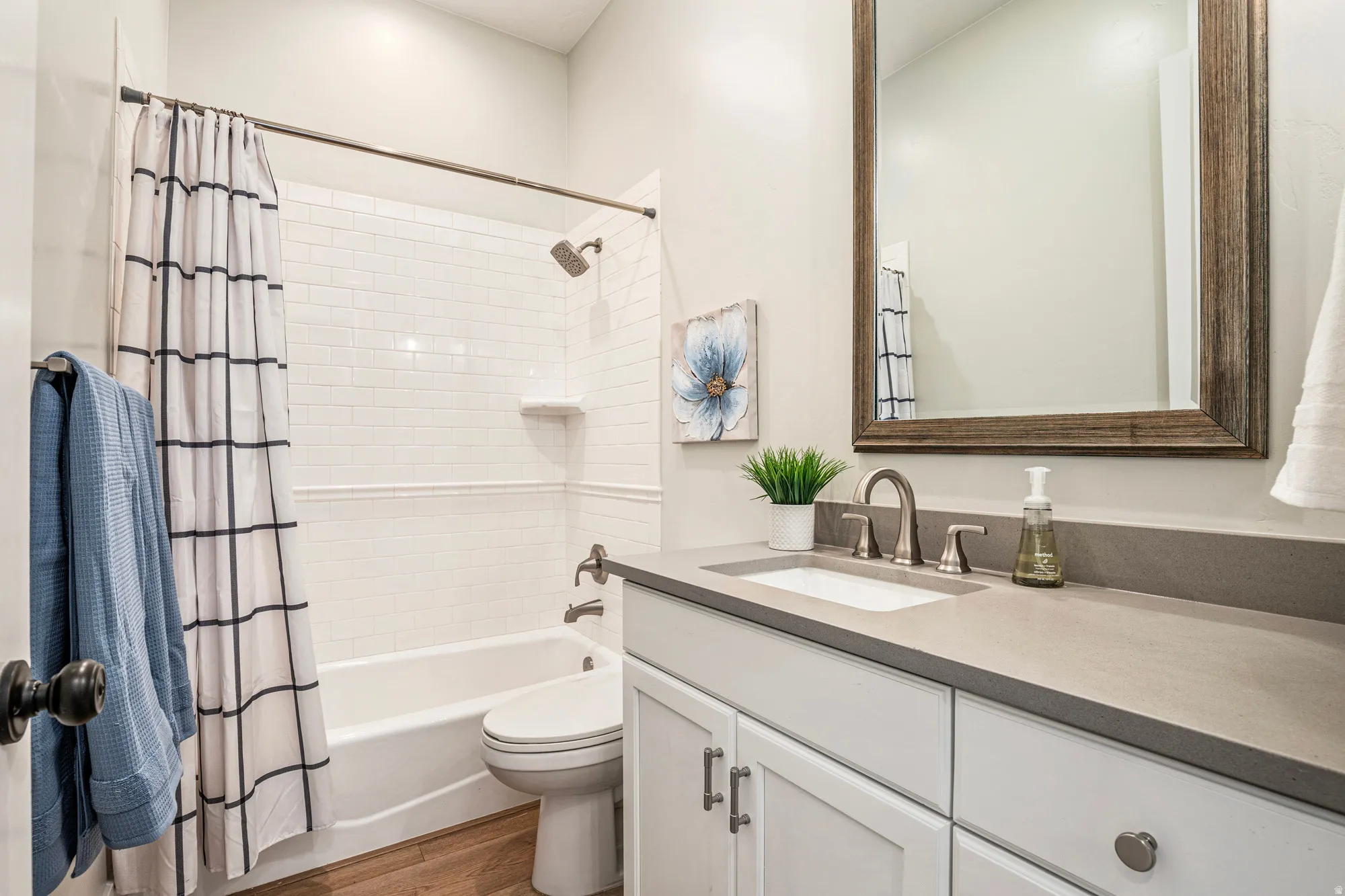 Bathroom featuring an integrated bathtub and shower with white subway tile surround, a built-in vanity with white shaker-style cabinetry, an undermount sink, and wood-finish flooring