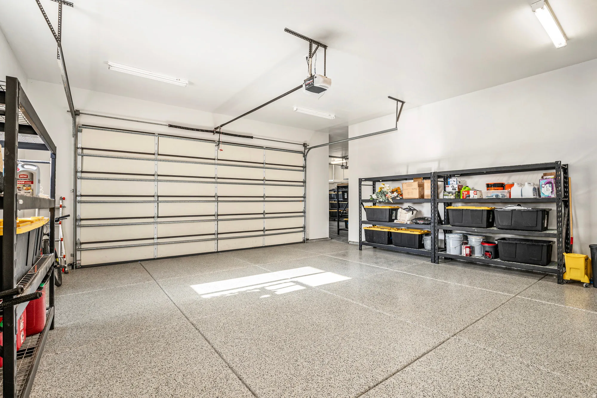 Spacious garage featuring a sectional garage door, epoxy-coated concrete flooring, overhead lighting, and built-in shelving systems