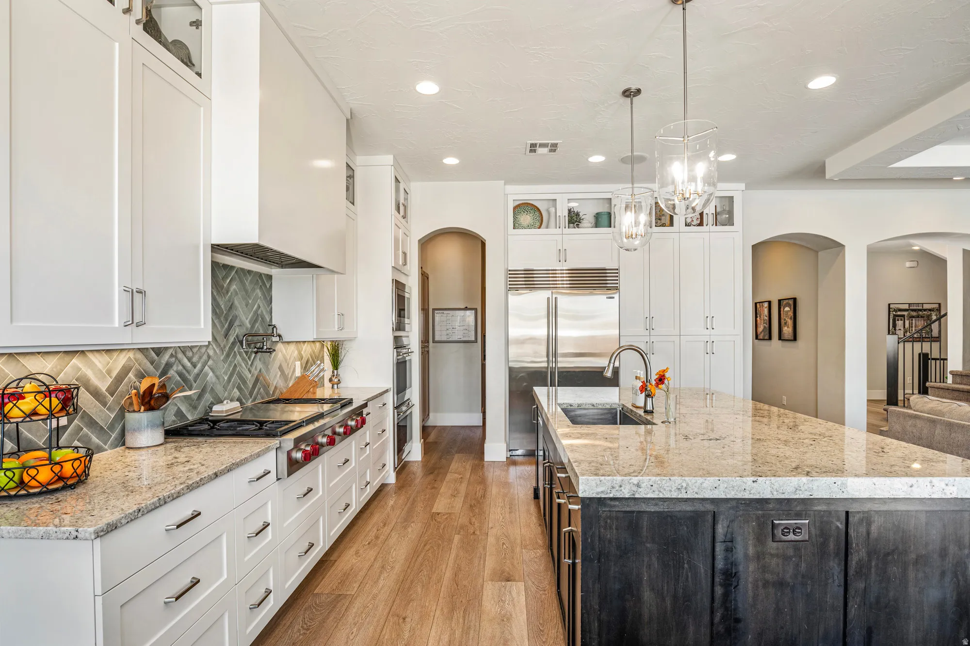 Gourmet kitchen featuring a large island with an undermount sink, pendant lighting, professional-grade stainless steel appliances, white cabinetry with polished hardware, and wood-finish flooring