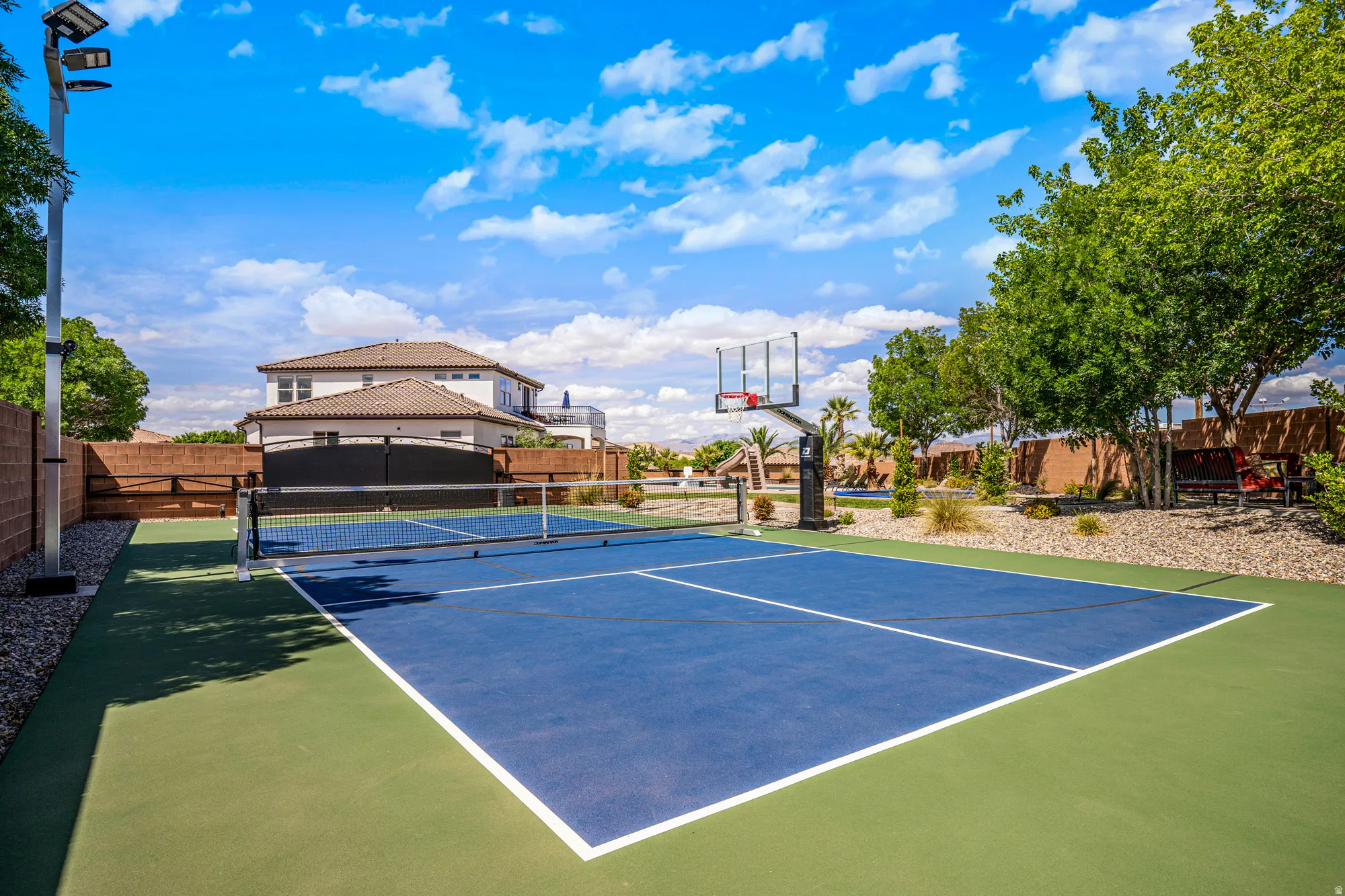 Multi-sport court featuring a blue playing surface with white boundary lines, green perimeter, and a net