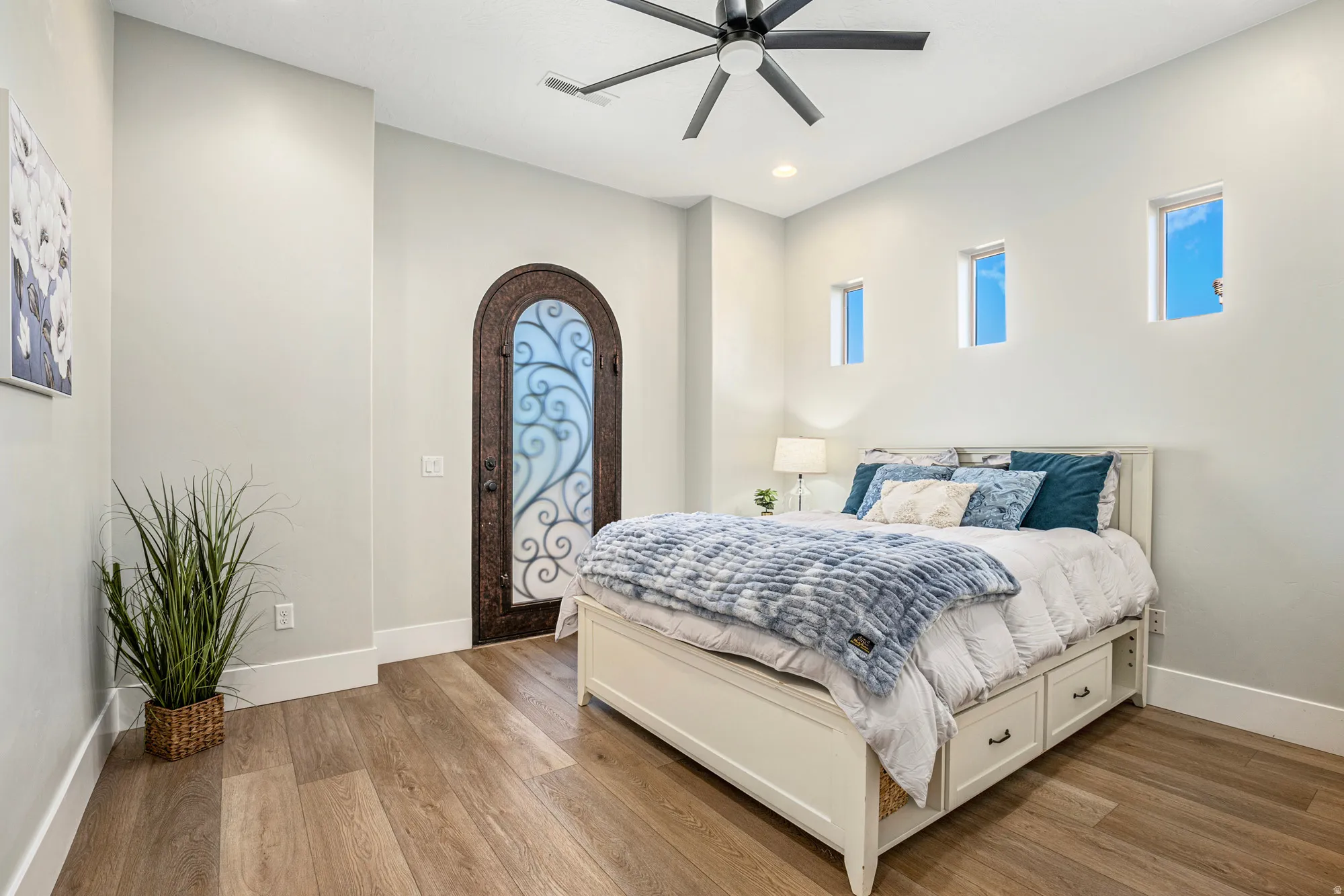 Interior space featuring wood-finish flooring, a decorative arched entry door with glass and wrought iron detailing, and three high vertical windows