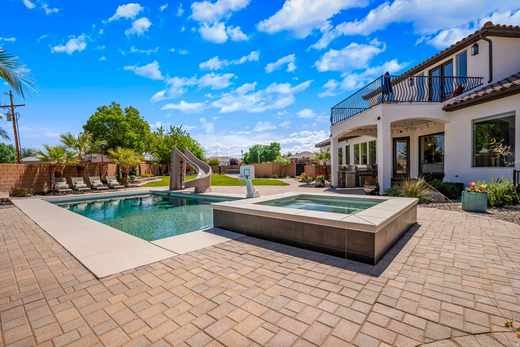 Expansive outdoor living area featuring a rectangular pool with an integrated slide, elevated spa, and extensive paver patio