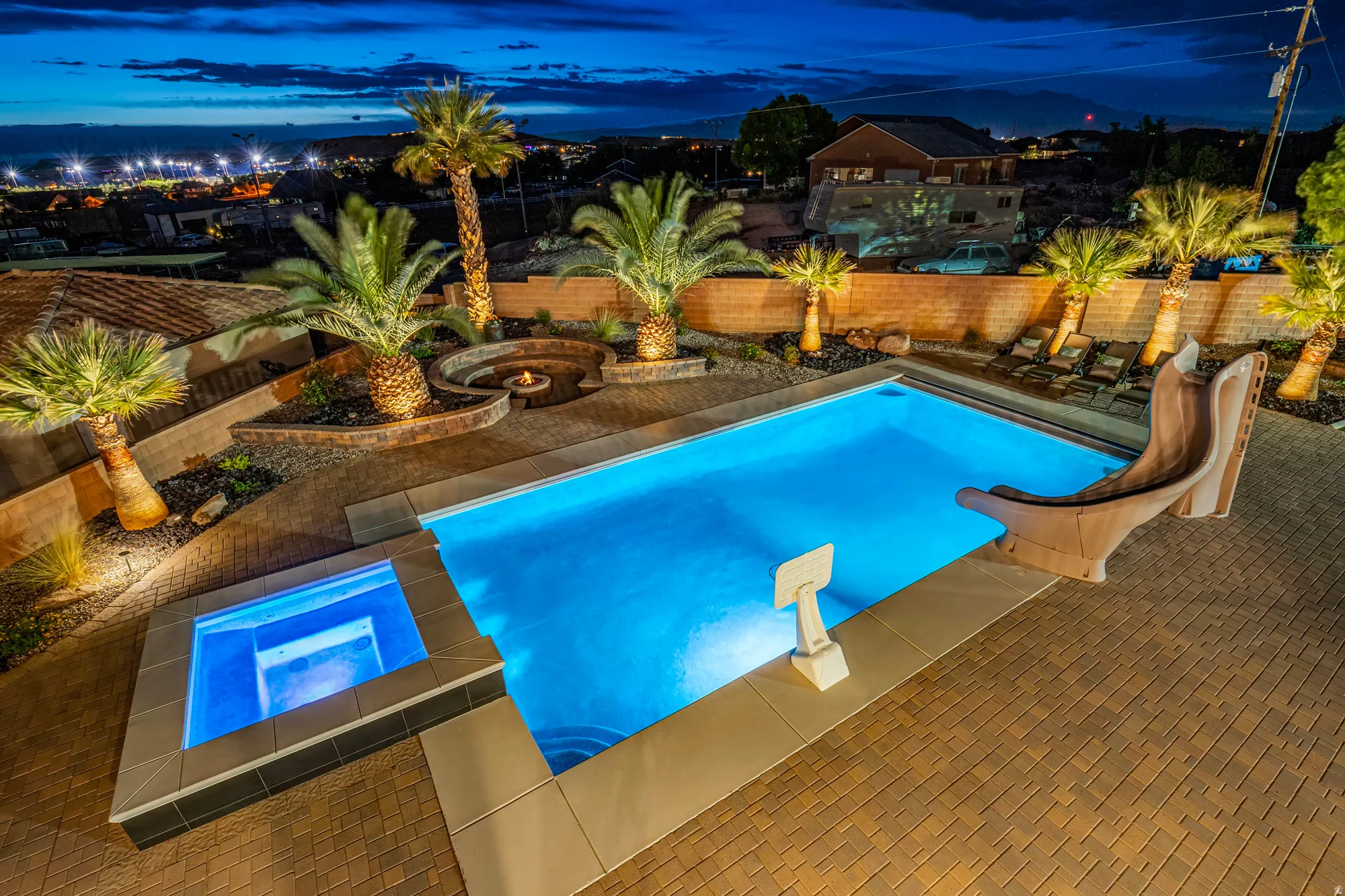 Resort-style backyard featuring a rectangular swimming pool with integrated slide, elevated spa, paver patio, and built-in fire pit