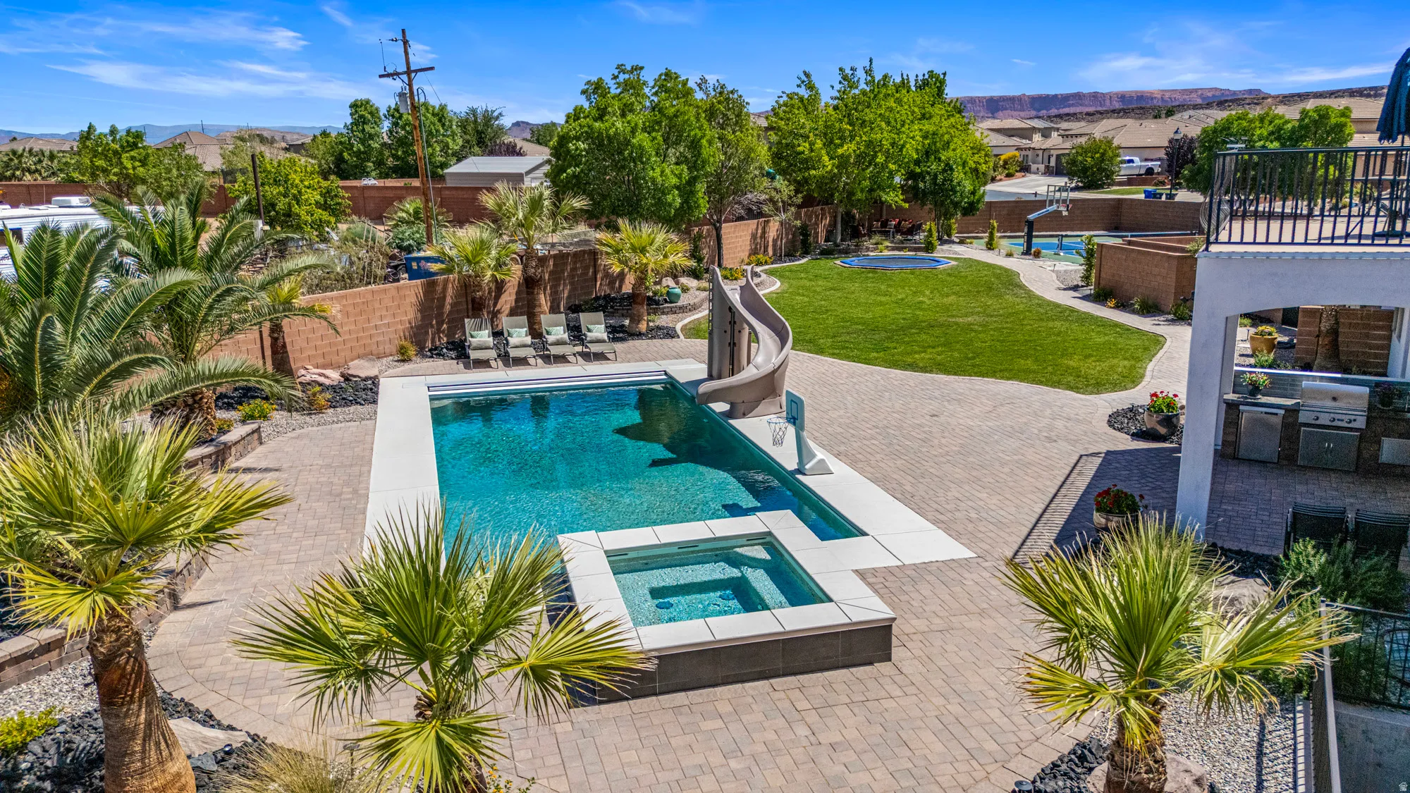 Expansive backyard oasis featuring a rectangular swimming pool with integrated spa and water slide, surrounded by paver patio areas