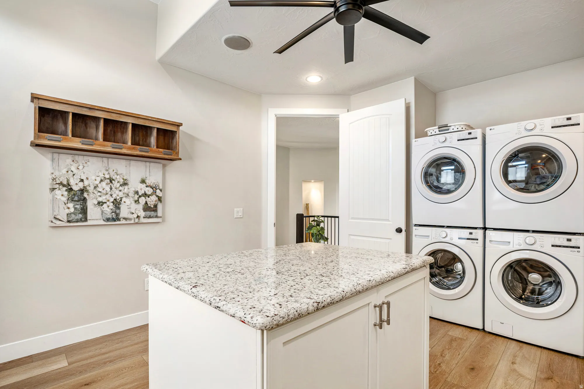Laundry area featuring a granite-topped island with cabinetry, stacked washers and dryers, wood-finish flooring, and a ceiling fan