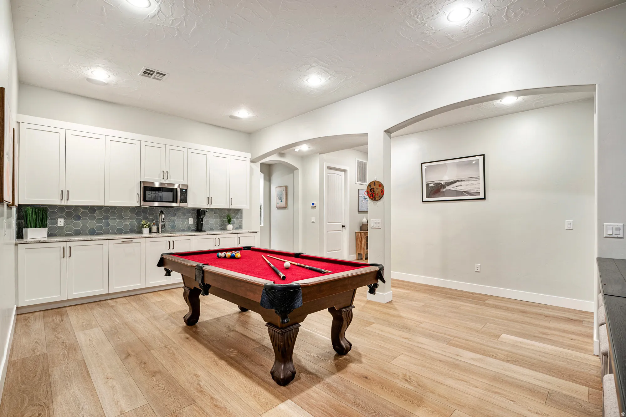 Spacious recreation room featuring wood-finish flooring, recessed lighting, and arched doorways
