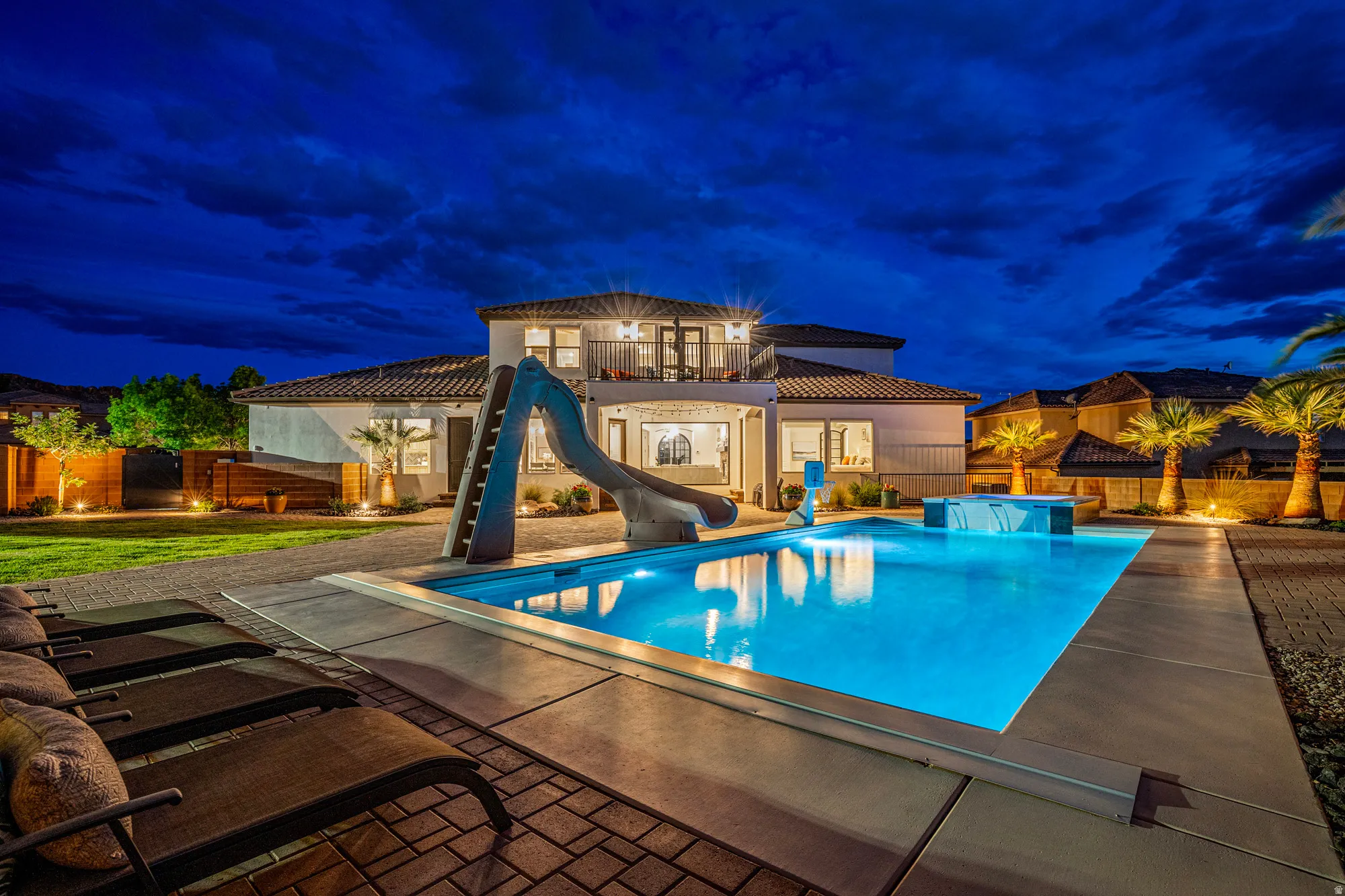Expansive backyard oasis featuring a rectangular pool with integrated slide, spa with waterfall feature, and ample concrete decking