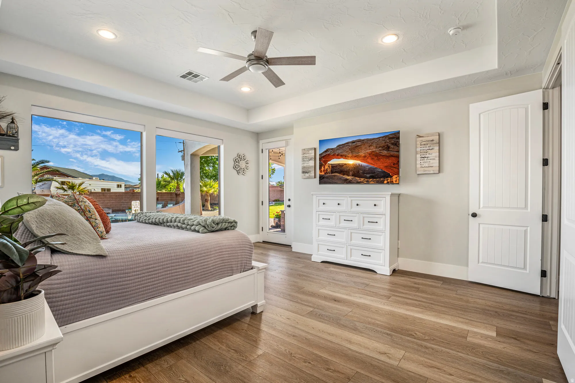 Spacious room featuring wood-finish flooring, a tray ceiling with recessed lighting, and a ceiling fan