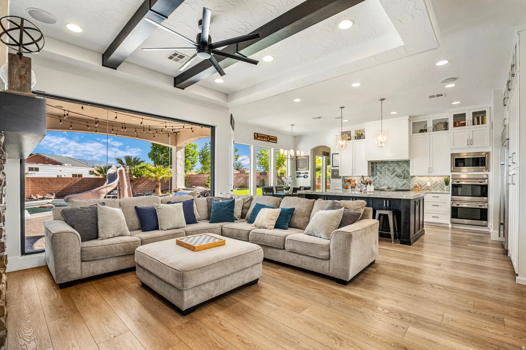 Expansive living area featuring large format glass doors, wood-finish flooring, and a coffered ceiling with exposed beams