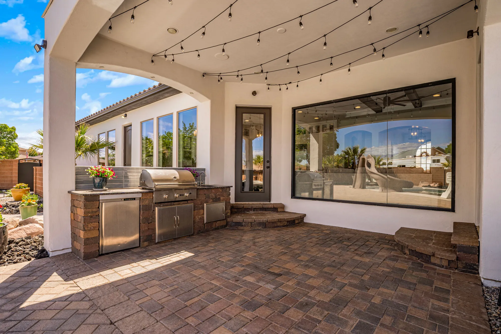 Covered patio featuring string lighting, paver flooring, and an outdoor kitchen with stainless steel appliances, brick veneer, and stone countertops