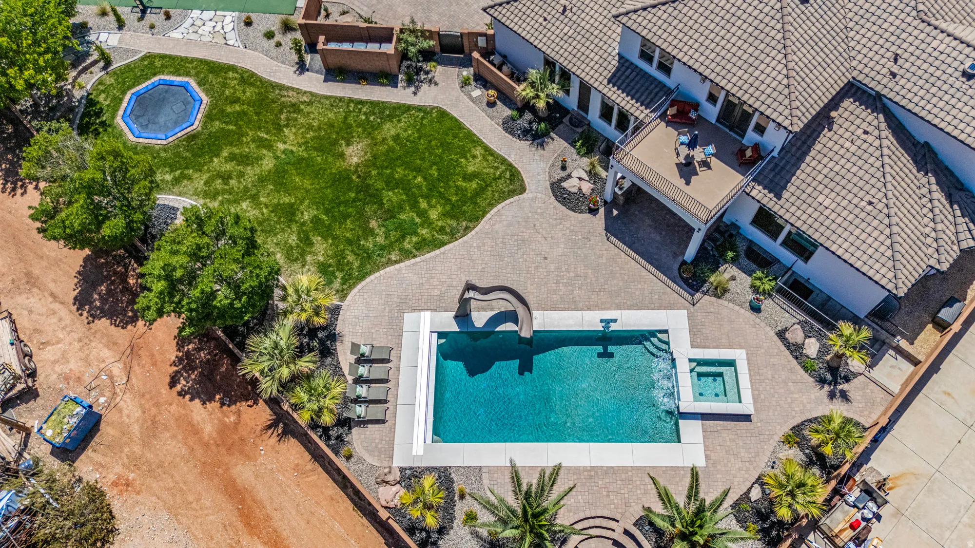 Expansive backyard retreat featuring a rectangular pool with integrated slide, accompanying hot tub, and paver patio