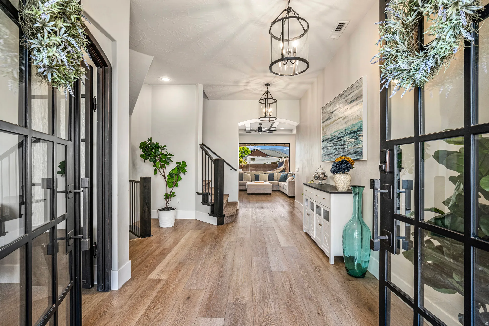 Entryway featuring double black grid-paneled doors, wood-finish flooring, two hanging circular chandeliers, and a white console table with a dark countertop