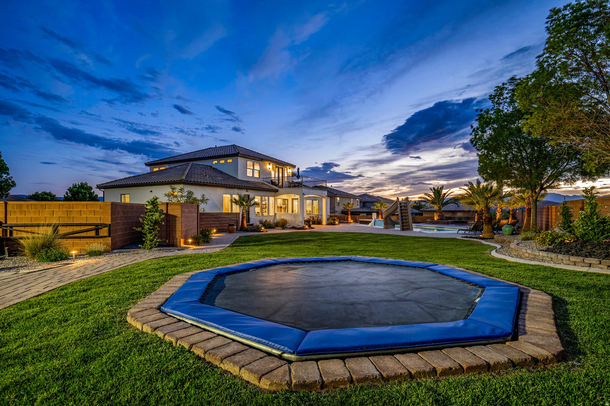 Spacious backyard featuring a manicured lawn, a built-in trampoline with paver surround, and mature landscaping