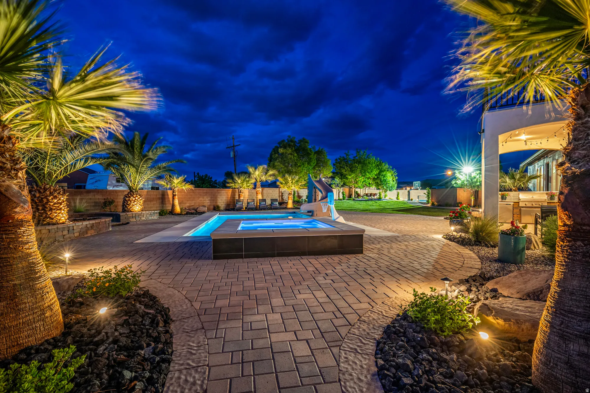 Expansive backyard featuring a paver patio with integrated accent lighting, a lighted pool with an elevated spa, established palm trees, and a covered outdoor living area