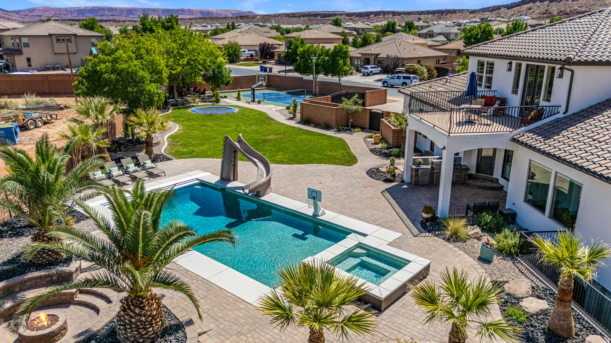 Expansive backyard featuring a large swimming pool with an integrated spa, a water slide, and an adjacent fire pit area