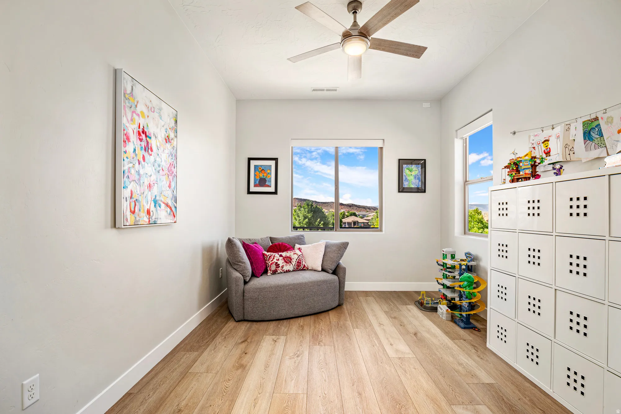 Bright room featuring wood-finish flooring, two large windows, a ceiling fan with integrated lighting, and high ceilings